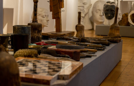 Wnętrze pracowni rzeźbiarskiej Alfonsa Karnego. Na blacie leżą szachownica i narzędzia rzeźbiarskie, z tyłu stoją gipsowe rzeźby.