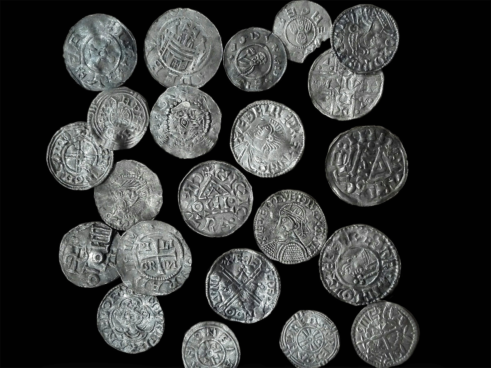 Dwadzieścia trzy srebrne monety pokryte wybitymi napisami oraz symbolami.