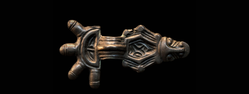 Metalowa zapinka, z czterema wypustkami na zakończeniu, cała pokryta ornamentem plastycznym, zakończona stylizowanym łbem.