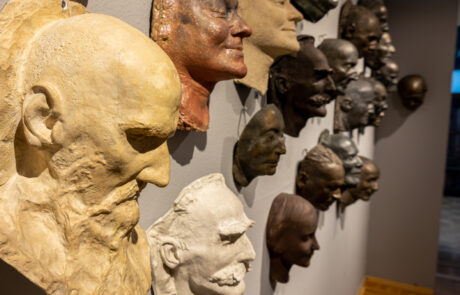Ściana z maskami pośmiertnymi. Wykonane są w glinie, gipsie i brązie. Ujęcie z lewej strony.