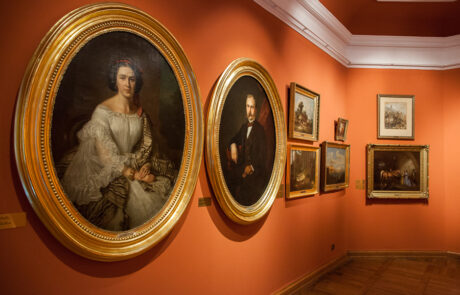 Widok na Salę Czerwoną. Od lewej dwa owalne portrety Karskich Józefa Simmlera w złotych ramach o dużych rozmiarach, w tle sześć mniejszych obrazów. Wsztskie pochodzą z XIX wieku.