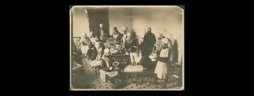Archiwalne zdjęcie ukazujące grupę kobiet podczas przygotowania posiłku. W tle duże drewniane drzwi.
