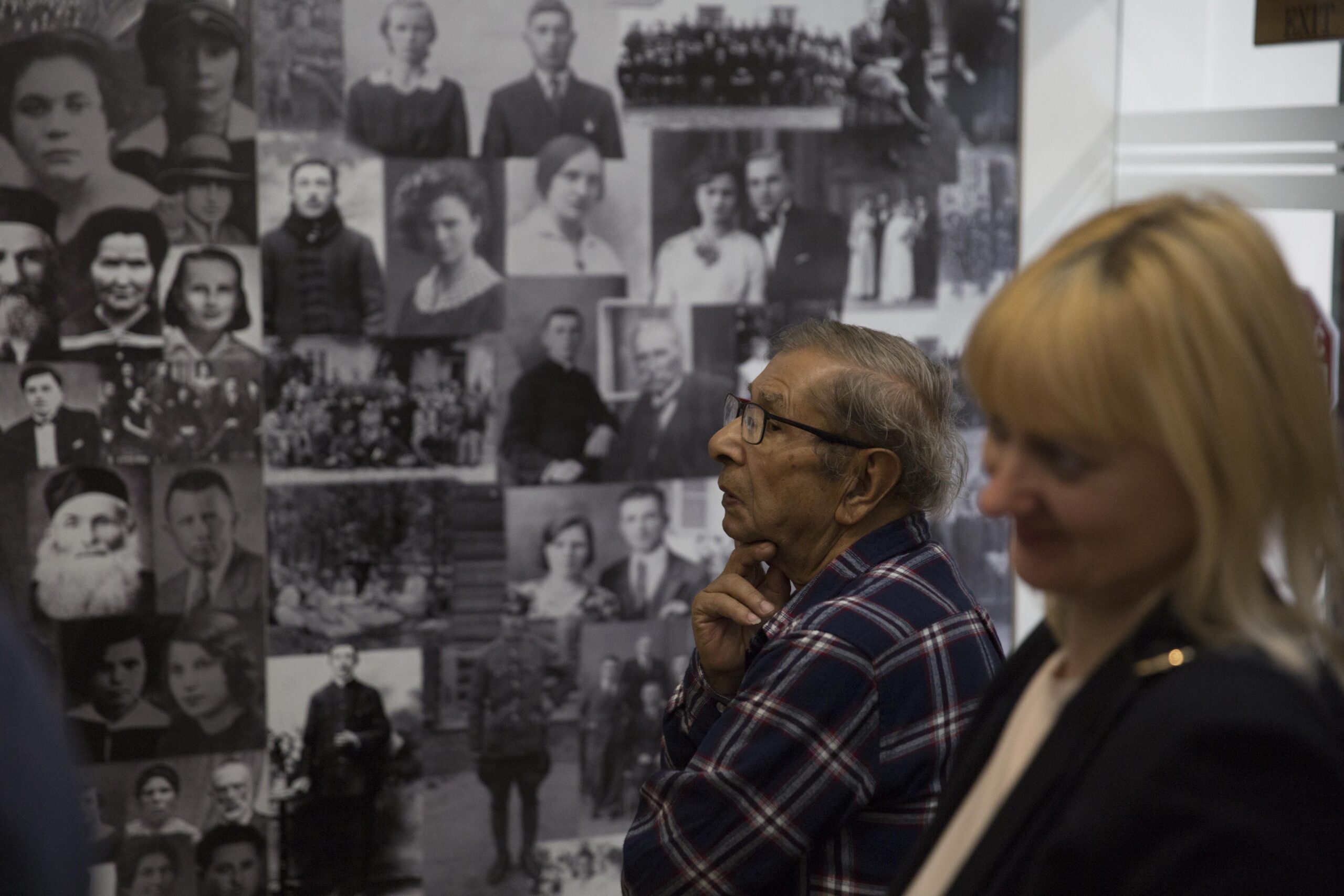 Na pierwszym planie dwie osoby oglądające wystawę w Domu Talmudycznym w Tykocinie. W tle ściana z kolażem złożonych z fotografii dawnych mieszkańców Tykocina.